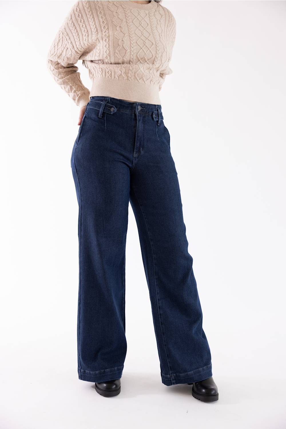 A person wearing dark blue wide-leg denim jeans and a cream cable-knit sweater, standing against a plain white studio background.