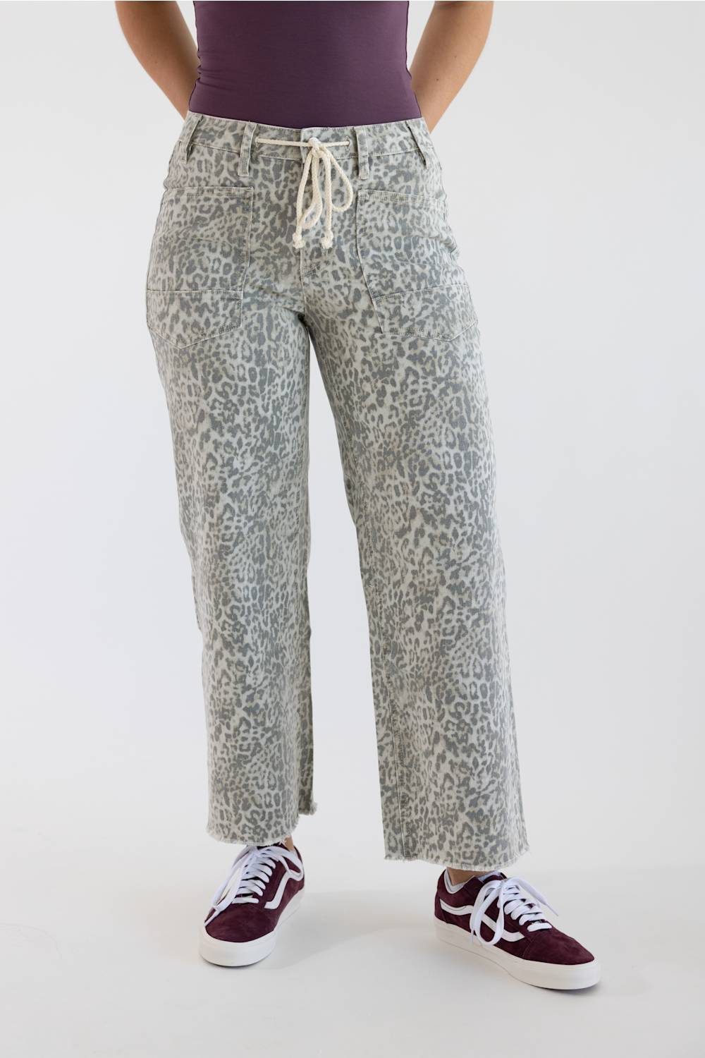 High-waisted wide-leg cropped jeans in a light grey leopard print, featuring a drawstring waist, raw hem, and styled with a dark top and sneakers.