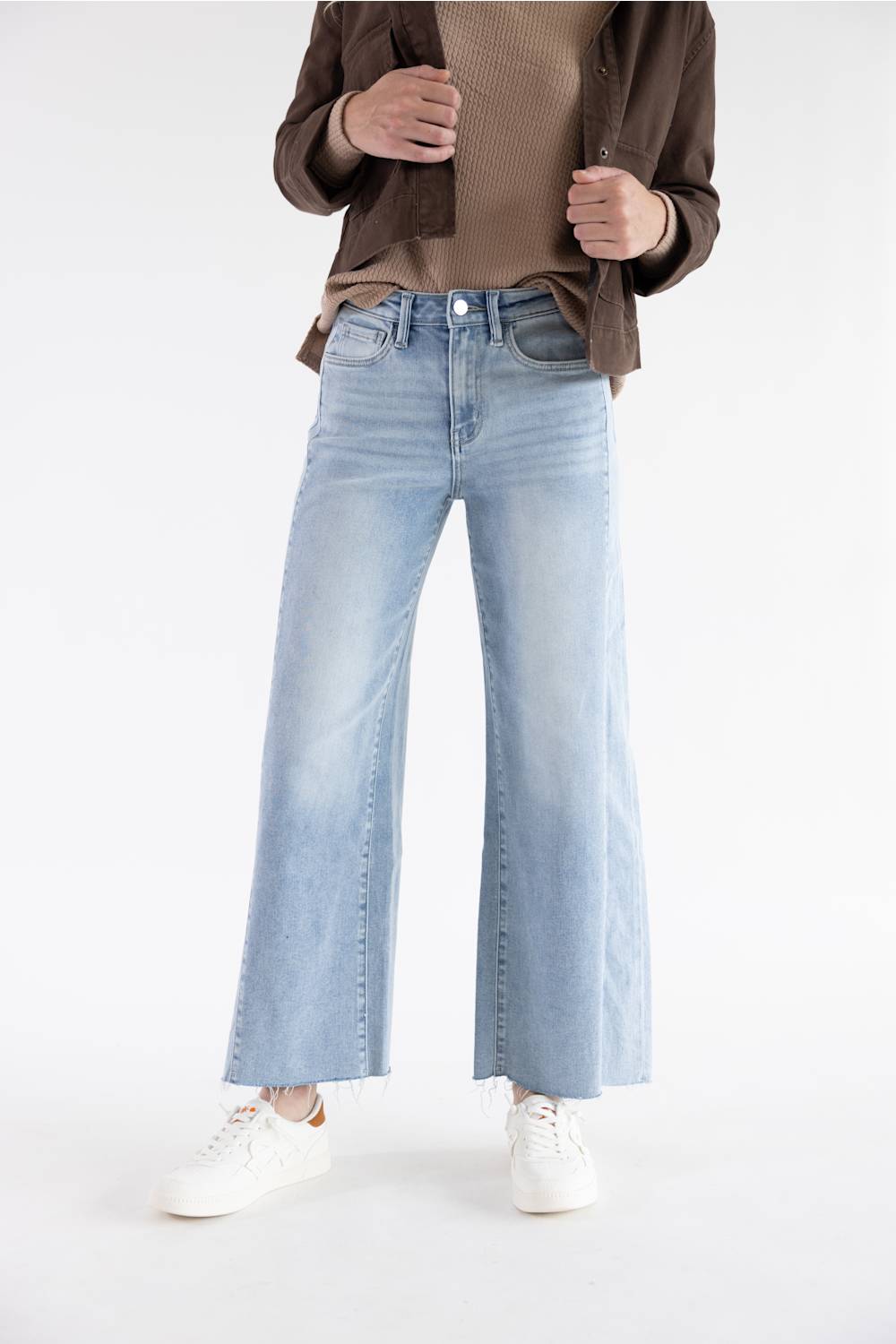 A model wearing light-wash blue wide-leg jeans with a faded wash, styled with a brown button-up shirt and white sneakers against a plain white studio background.