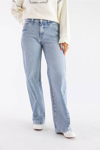 A person wearing light-wash blue straight-leg jeans, a cream ribbed sweater, and white shoes, photographed against a plain light gray studio background.