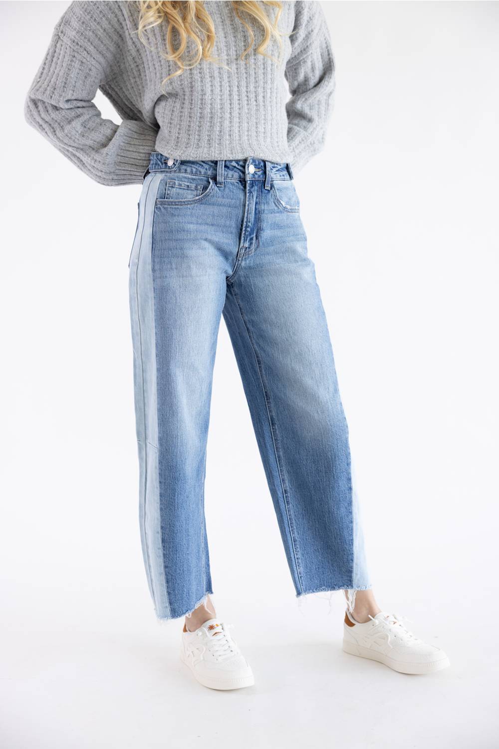A person wearing light-wash blue wide-leg jeans with a gray ribbed knit sweater and white sneakers, photographed against a clean white studio background.