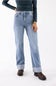 A model wearing light-wash blue denim jeans with rolled cuffs, paired with a dark green long-sleeve top and brown boots, shown from the waist down on a white studio background.