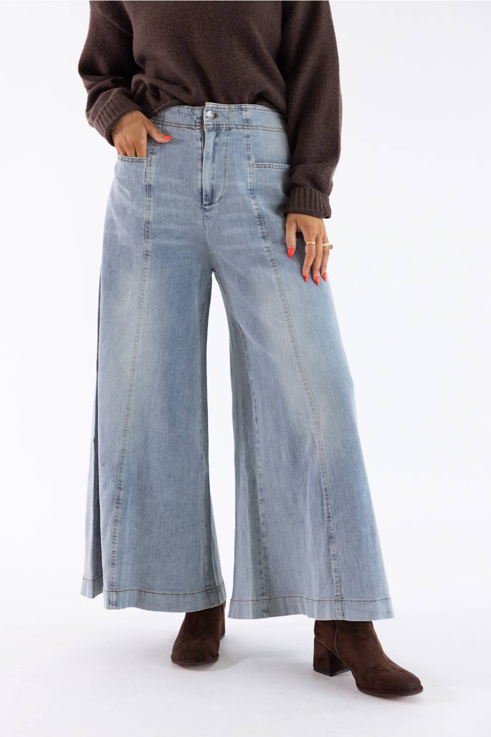 A model wearing light-wash wide-leg denim jeans, styled with a dark brown knit sweater and brown heeled ankle boots against a plain white studio background.