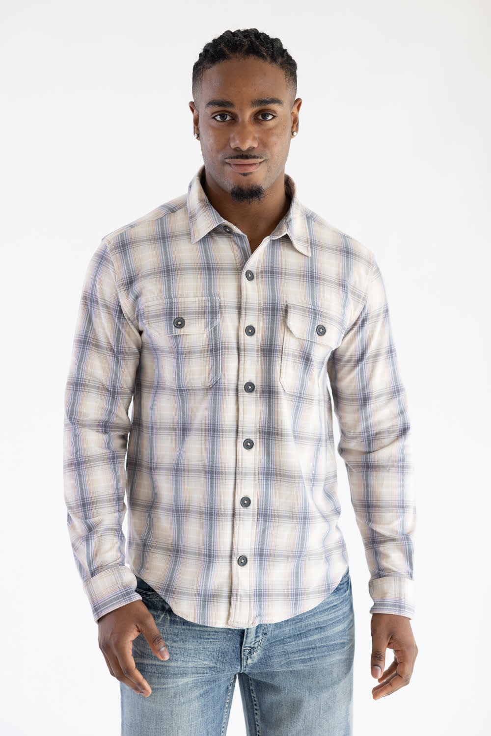 Front-facing three-quarter view of a man wearing the Hallstatt Knit Button Up Flannel Shirt in Sand with a plaid pattern in blue, beige, and gray, paired with light-wash jeans against a white backdrop.