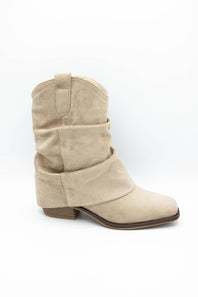 A single light beige suede ankle boot with a slouchy western design, featuring a stacked wrap-around strap and a low block heel, shown against a plain white background.