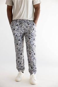 A person wearing gray and white camouflage jogger pants with a light beige t-shirt and white sneakers, shown from the waist down against a plain white studio background.