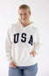 Woman wearing an ivory Reflex USA fleece hoodie with dark blue "USA" lettering across the chest.