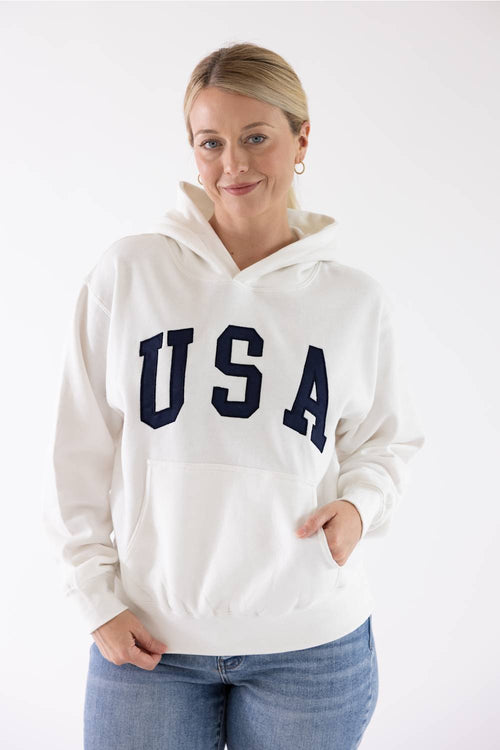 Woman wearing an ivory Reflex USA fleece hoodie with dark blue "USA" lettering across the chest.