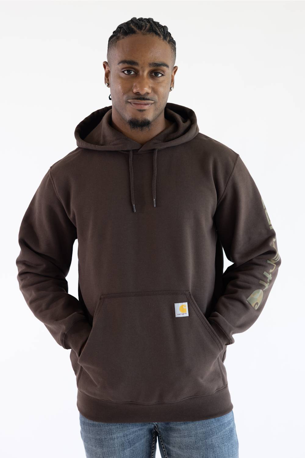 Front-facing view from the waist up of a male model against a plain white background, looking forward while wearing a dark clove brown Carhartt hooded sweatshirt with a small logo patch on the front pocket, paired with medium wash denim jeans.