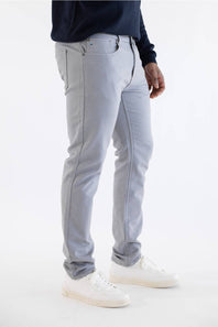 A person wearing light gray slim-fit jeans, a dark navy long-sleeve top, and white sneakers, shown from the waist down against a plain white studio background.