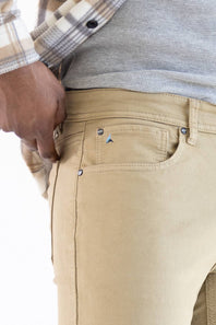 Close-up of a person wearing tan chino pants, with a gray ribbed shirt and a beige-and-white plaid flannel shirt visible. The photo focuses on the back pocket and waist area of the pants.