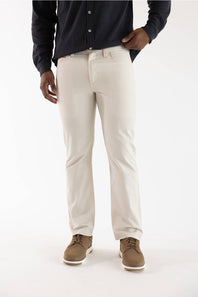 A person wearing off-white straight-leg chino pants, a dark navy long-sleeve button-up shirt, and brown suede shoes, standing against a plain white studio background.
