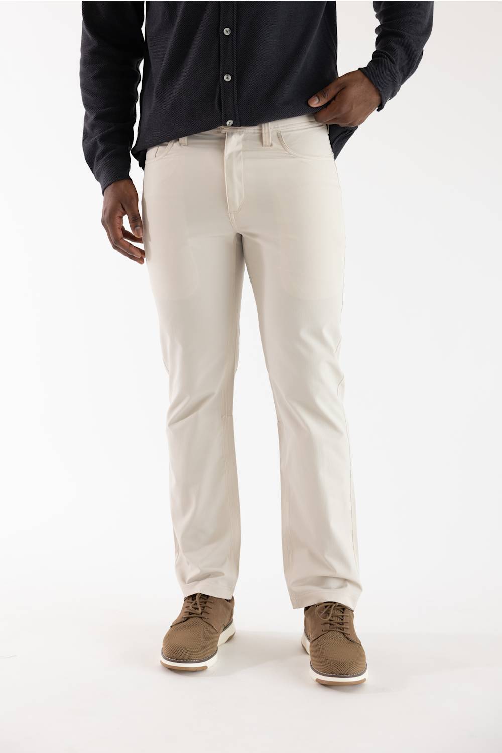 A person wearing off-white straight-leg chino pants, a dark navy long-sleeve button-up shirt, and brown suede shoes, standing against a plain white studio background.