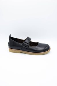 A single black leather Mary Jane shoe with a hook-and-loop strap and a tan sole, photographed on a white background.