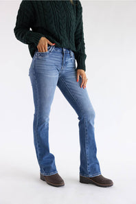 A model wearing blue flare jeans, a dark green cable-knit sweater, and brown boots, standing against a plain white studio background.
