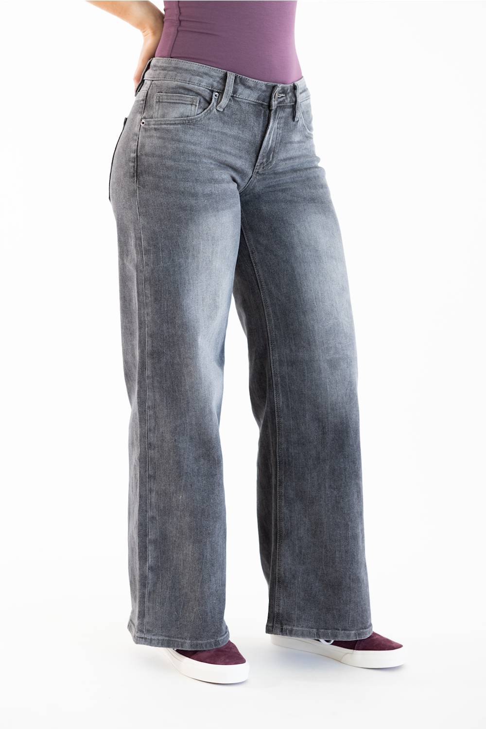 A person wearing wide-leg gray denim jeans with a faded wash, paired with a purple top and burgundy sneakers, shown from the waist down on a white studio background.