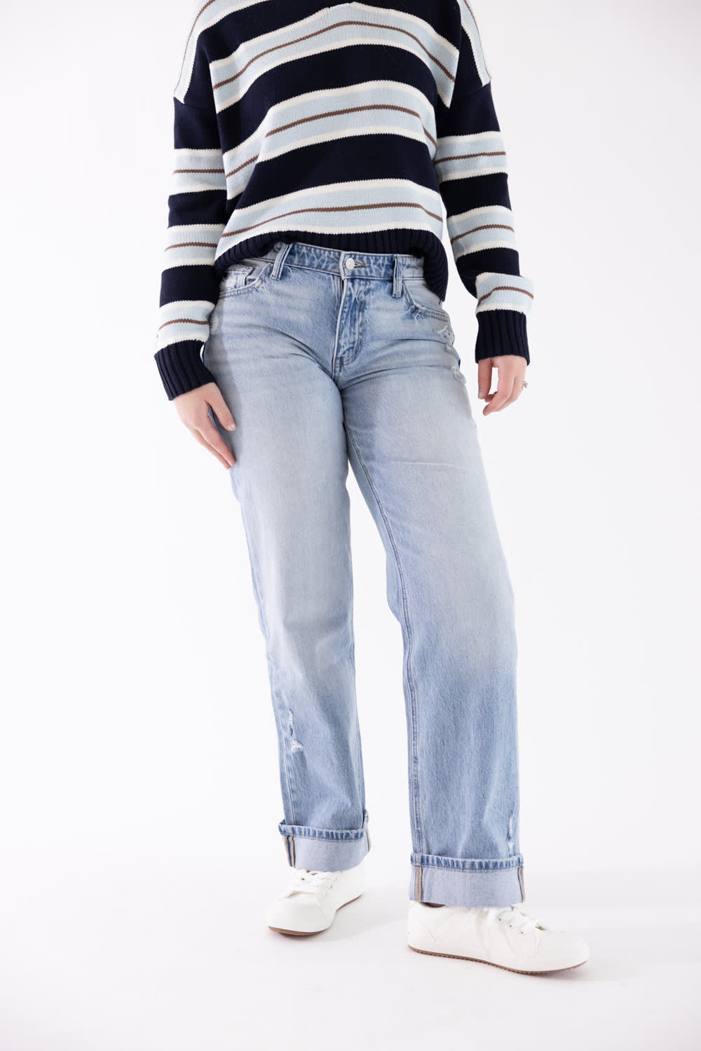 A person wearing light-wash blue straight-leg jeans, a navy and white striped sweater, and white sneakers, photographed against a plain white studio background.