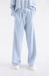 A person wearing light blue and white striped lounge pants with a drawstring waist, paired with a matching striped top and white slip-on shoes, shown against a plain light gray studio background.