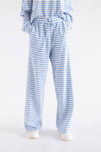 A person wearing light blue and white striped lounge pants with a drawstring waist, paired with a matching striped top and white slip-on shoes, shown against a plain light gray studio background.