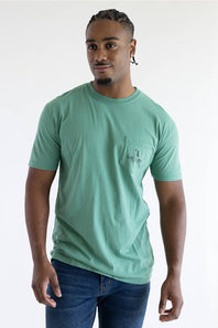 A man wearing a light green shirt with a graphic saying Local Boy Outfitters with a dog and a half moon.