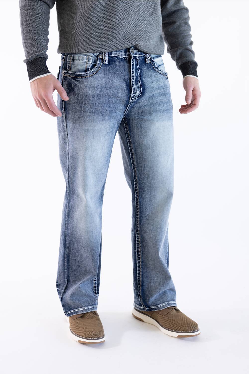 Front view of a male model wearing True Luck Mac Loose Straight medium-wash jeans with light fading and whiskering, a grey long-sleeve sweater, and brown casual shoes against a plain white background.