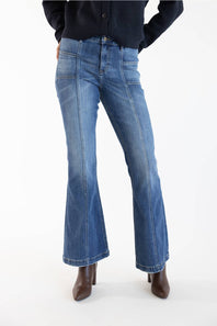 A person wearing medium-dark denim flare jeans with a dark navy top and brown pointed-toe heeled boots, photographed against a clean white studio background.