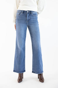 A person wearing medium-wash blue wide leg jeans with a white ribbed sweater and brown heeled ankle boots, shown from the waist down against a plain white studio background.