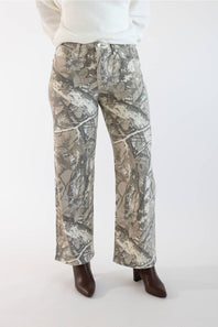 A person wearing camouflage wide-leg pants with a white ribbed sweater and dark brown pointed-toe boots, shown from the waist down against a plain light background.