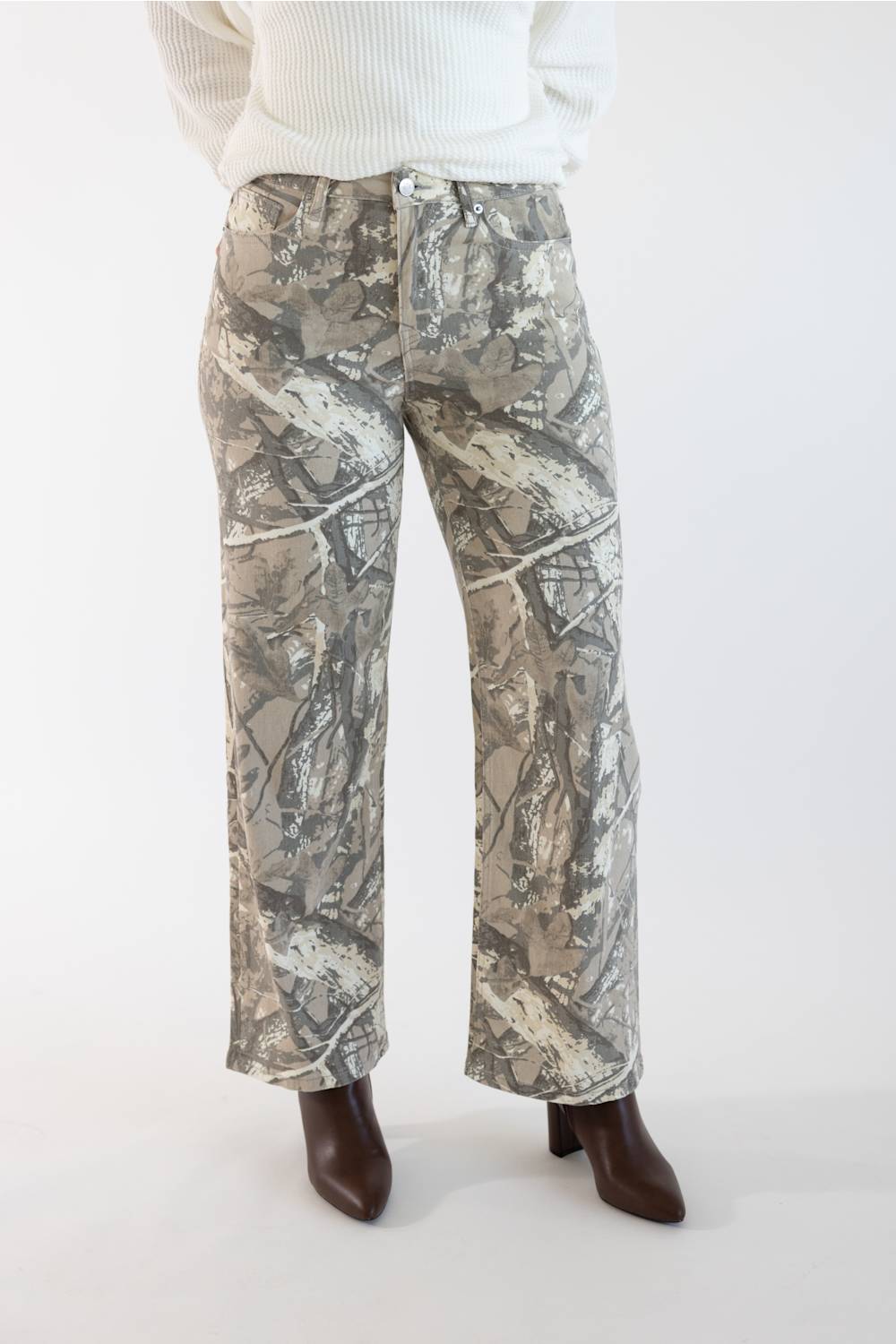 A person wearing camouflage wide-leg pants with a white ribbed sweater and dark brown pointed-toe boots, shown from the waist down against a plain light background.