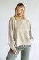 A woman modeling a beige acid-wash crewneck sweatshirt with unique sleeve cutouts, paired with olive green pants, against a plain light gray background.