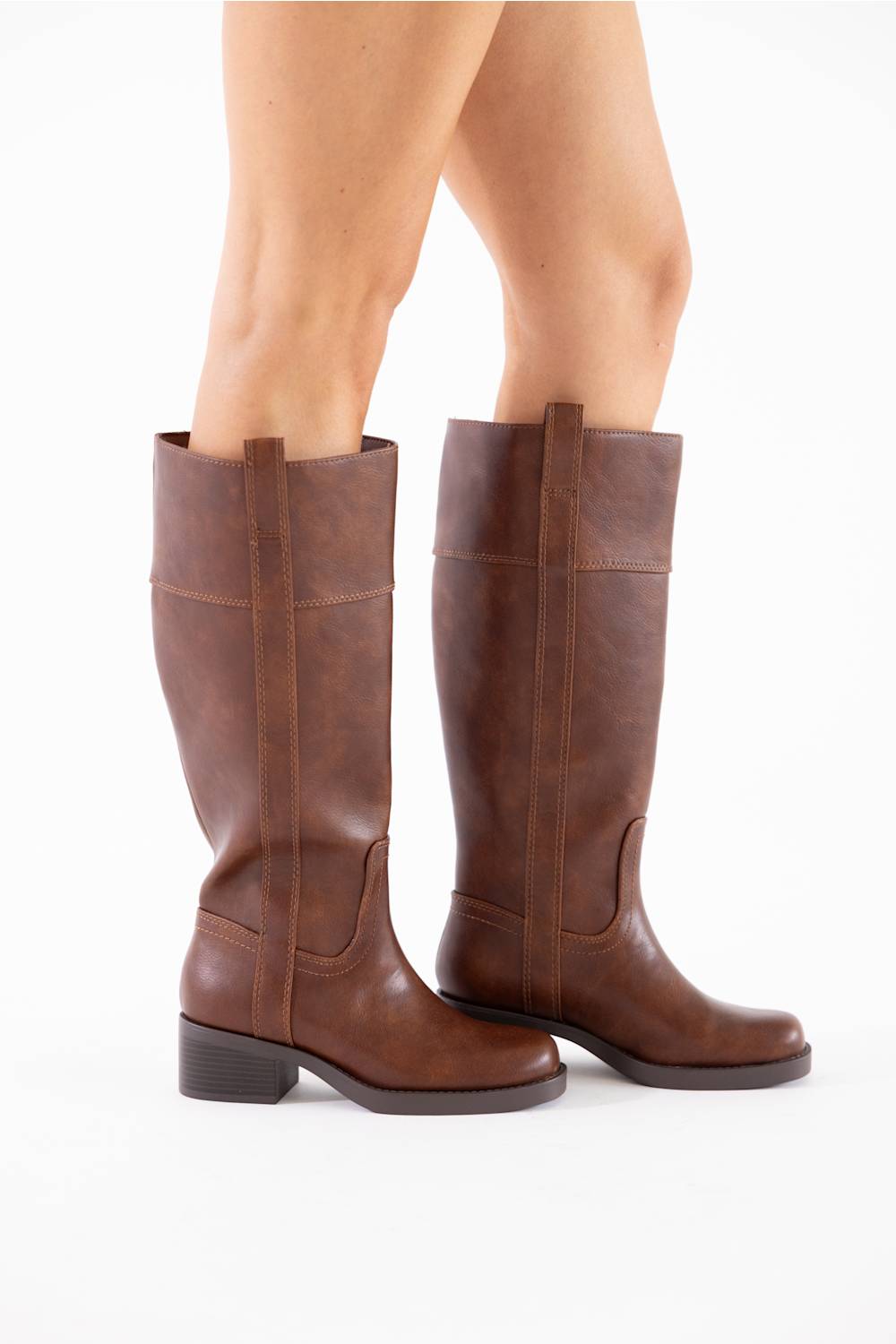 A pair of knee-high brown leather boots with low block heels, shown on a model's feet against a plain white background.