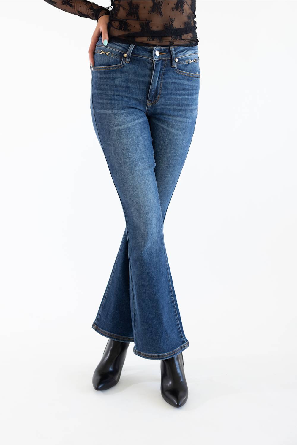 A model wearing a pair of medium-wash blue flare jeans with black pointed-toe ankle boots, shown from the waist down on a white studio background.