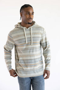 A man wearing a long-sleeve striped hoodie with a kangaroo pocket, featuring horizontal stripes in beige, brown, and gray on an off-white base, paired with blue jeans against a plain white background.