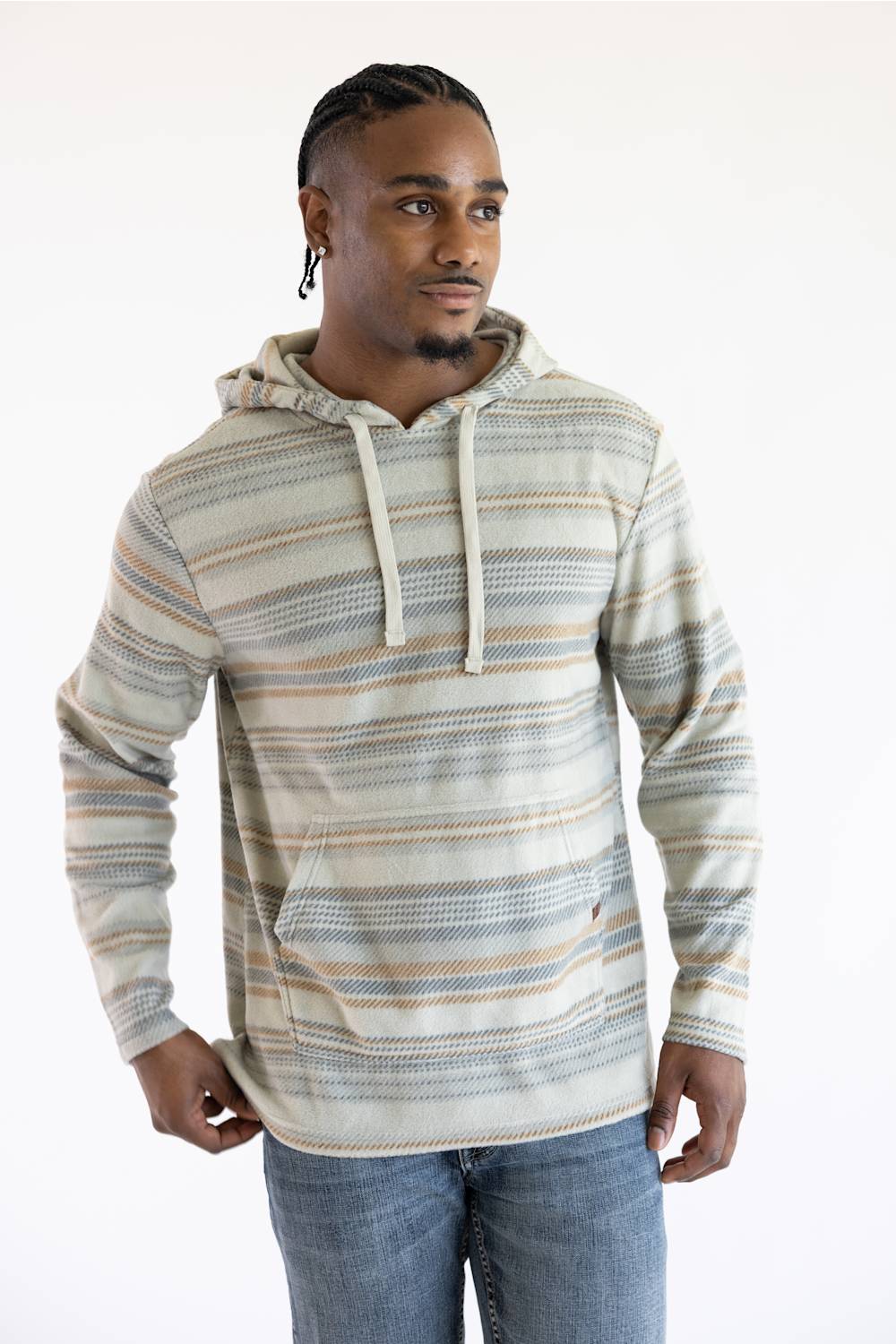 A man wearing a long-sleeve striped hoodie with a kangaroo pocket, featuring horizontal stripes in beige, brown, and gray on an off-white base, paired with blue jeans against a plain white background.