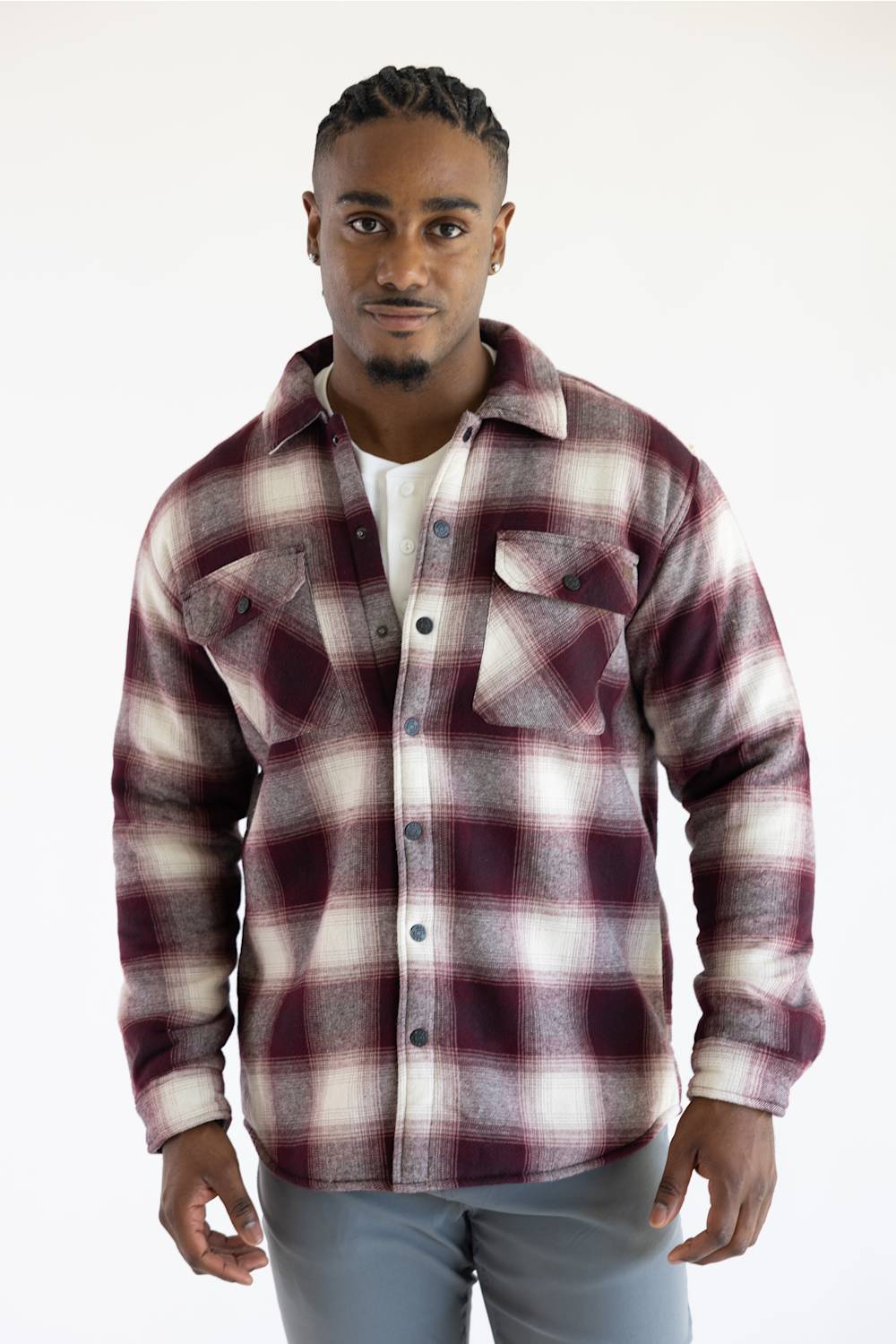 A man wearing a long-sleeve button-up plaid flannel shirt in burgundy and white, paired with gray pants, against a plain white studio background.