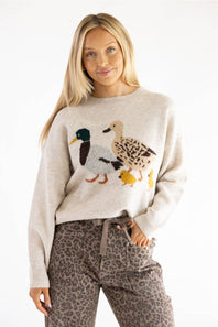A woman modeling a cream-colored knit sweater featuring a detailed embroidered duck design on the front, paired with leopard-print pants against a plain white background.