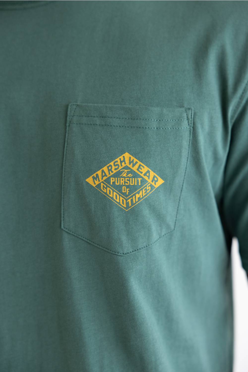 A close-up of a teal green long-sleeve pocket t-shirt featuring a yellow diamond-shaped embroidered logo on the chest pocket that reads 'MARRSWEAR PURSUIT OF GOOD TIMES'.