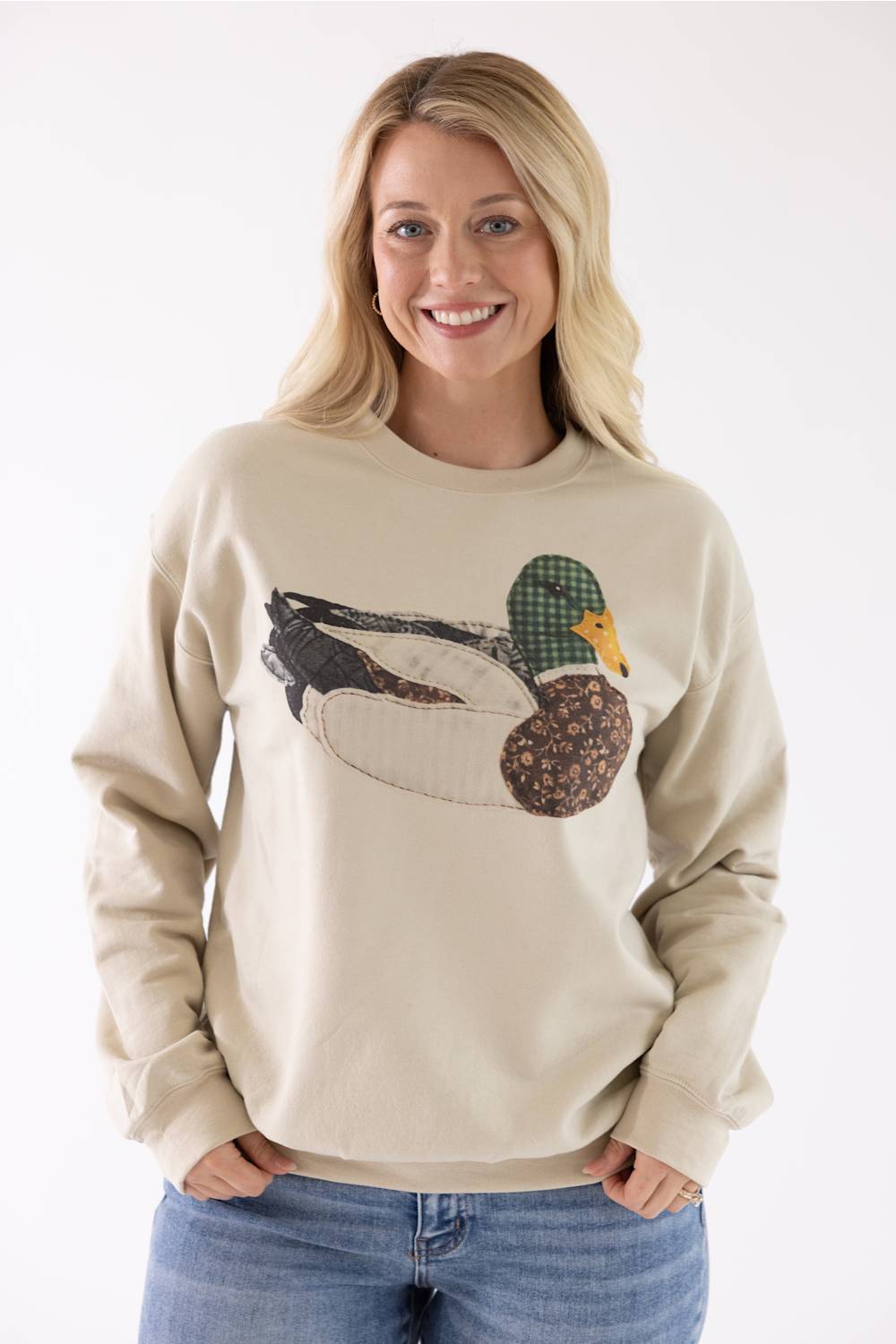 Model wearing the Mallard Duck Sweatshirt for Women in Cream, featuring a crew neckline, long sleeves, and a detailed patch-stitch duck graphic on the front.