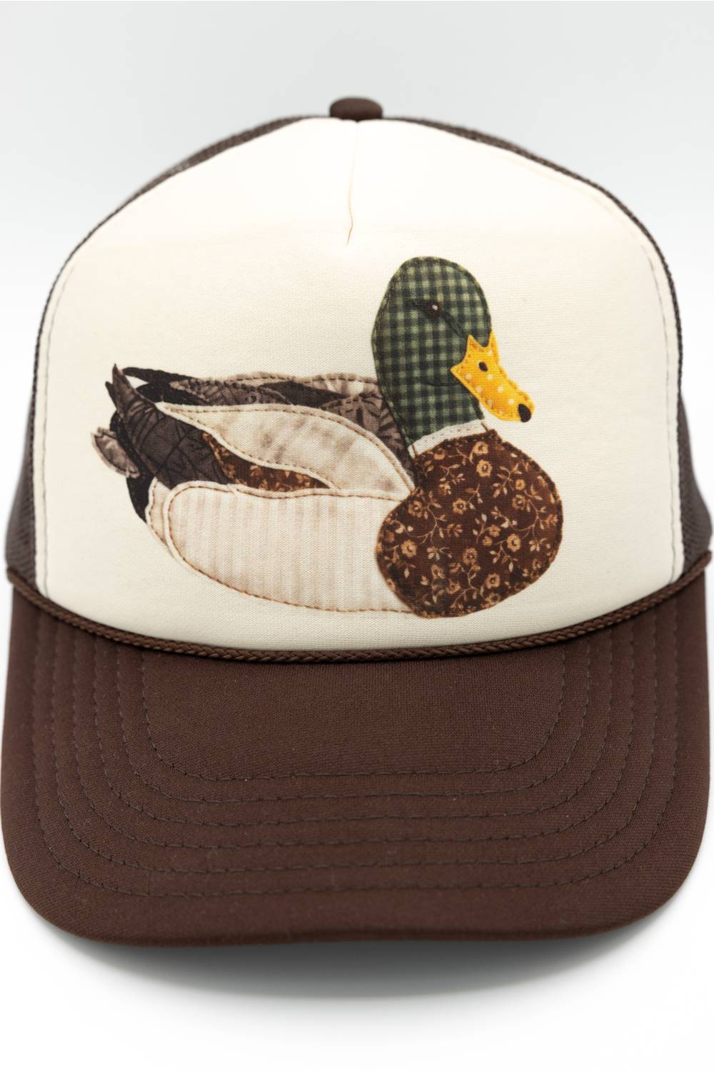 C.C. Mallard Duck Trucker Hat for Women in Cream and Brown. Front product shot showing the white foam front panel with a detailed patch-stitch mallard duck graphic, brown mesh back, and brown brim.