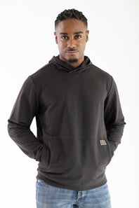 Model wearing a dark raven black long-sleeve hooded sweatshirt featuring a crossover neckline, front kangaroo pocket, small woven brand patch near the hip, paired with blue jeans against a white background.