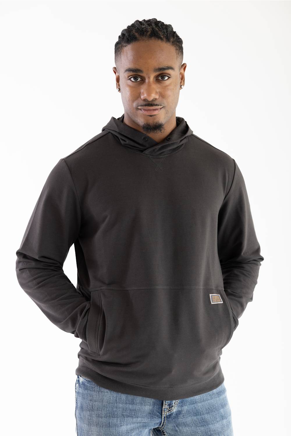 Model wearing a dark raven black long-sleeve hooded sweatshirt featuring a crossover neckline, front kangaroo pocket, small woven brand patch near the hip, paired with blue jeans against a white background.