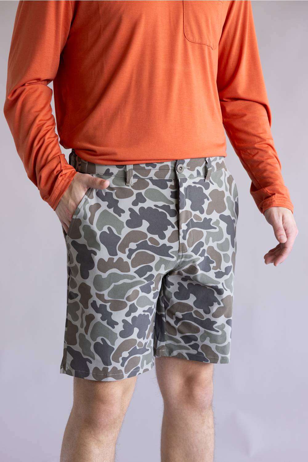 Marsh Wear Prime Hagood 8” Shorts for Men in Green Mallard Camo; Person wearing an orange long-sleeve shirt and camouflage shorts on a plain background