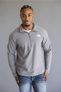 A man wearing a light gray quarter-zip fleece pullover by The North Face, paired with blue jeans, standing against a solid gray studio background.