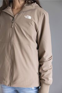 A person wearing a taupe-beige hooded zip-up jacket by The North Face, paired with light blue jeans, shown against a plain gray background.