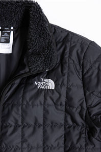 Close-up of a black quilted puffer jacket with a black sherpa fleece collar and a white embroidered The North Face logo on the chest.