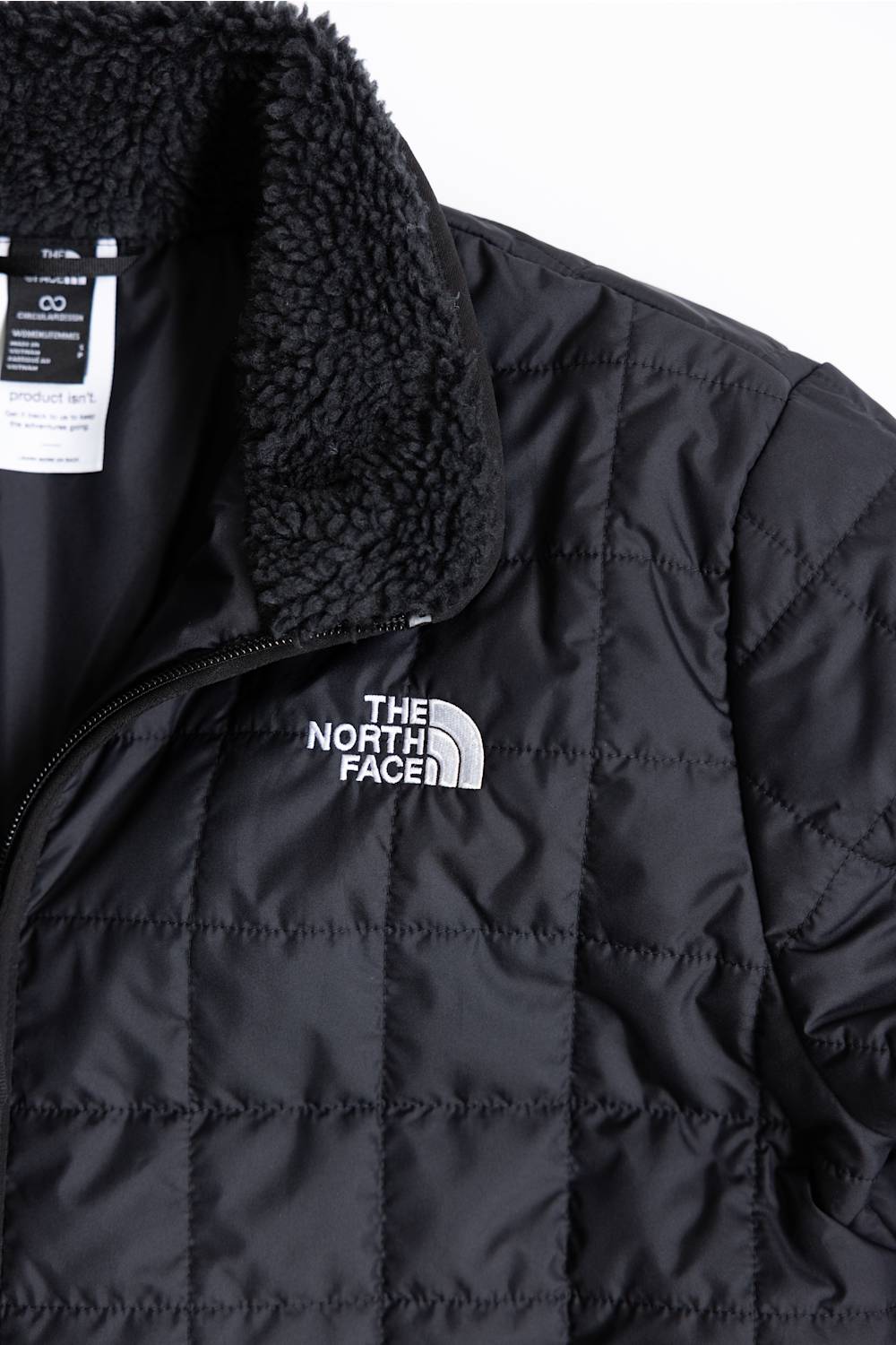 Close-up of a black quilted puffer jacket with a black sherpa fleece collar and a white embroidered The North Face logo on the chest.