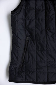 Close-up of a black quilted puffer vest with horizontal stitching and a vertical zippered pocket on a white background.