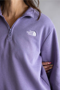 A close-up of a person wearing a lavender purple quarter-zip sweatshirt by The North Face, showing the white embroidered logo on the chest.