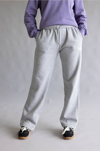 A person shown from the back wearing light heather gray sweatpants, a lavender sweatshirt, and black sneakers against a plain light gray studio background.