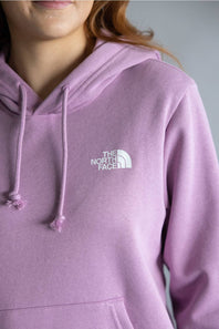 A close-up of a person wearing a lavender-purple pullover hoodie with white drawstrings and a white embroidered 'THE NORTH FACE' logo on the left chest, set against a neutral gray background.